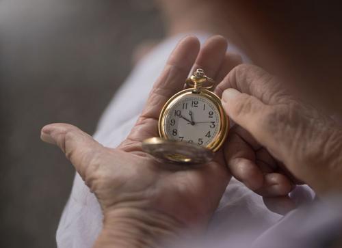 Mani vecchie che tengono un orologio da tasca aperto.