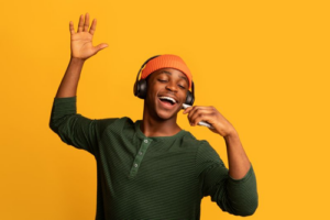 man-in-orange-beanie-black-headphones-and-a-green-jumper-singing-with-their-eyes-closed-in-front-of-a-mustard-yellow-background-m.png