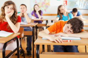 Fotografia di sei bambini che sembrano molto annoiati, seduti a scrivanie scolastiche di legno