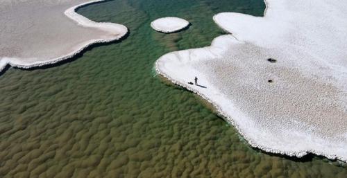 small-human-figure-standing-on-a-white-rocky-surface-near-a-green-pool-of-water-with-underwater-mounds-m-1.jpg