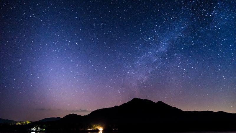 Una montagna scura è profilata in questa foto dietro il cielo stellato con il bagliore della luce zodiacale e il bagliore della Via Lattea che creano una forma a V