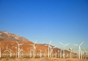 row-of-wind-turbines-under-a-blue-sky-orange-brown-mountain-in-the-background-m.jpg