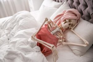 skeleton-in-a-pink-silk-tank-top-and-head-towel-lounging-in-bed-skull-resting-on-its-hand-m.jpg