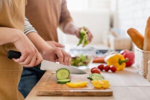 Immagine ravvicinata ritagliata di tagliere e coppia che taglia verdure insieme in cucina,