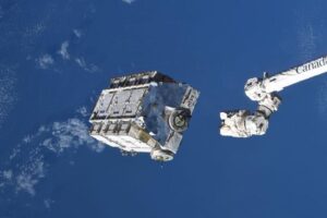 porzione del braccio robotico Canadarm che rilascia una struttura bianca a forma di scatola con le batterie