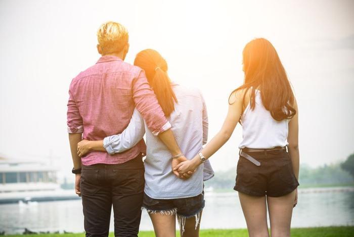 a-couple-with-their-arms-around-each-other-but-the-man-is-holding-hands-with-another-woman-behind-his-partner-s-back-m.jpg