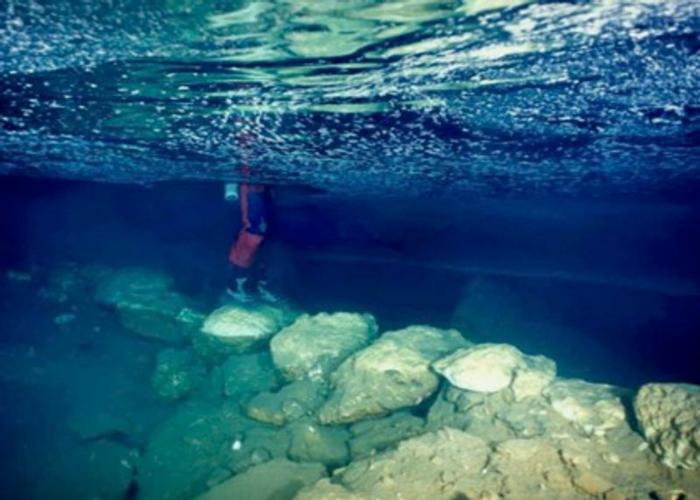 ponte sottomarino, fotografato da appena sotto la superficie; le gambe di qualcuno sono visibili mentre stanno sulle pietre del ponte