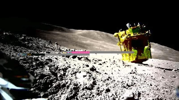 SLIM come si trova attualmente sulla superficie della Luna, visto da uno dei suoi rover. Il lander dorato è capovolto con i razzi puntati verso l'alto e i pannelli solari in ombra