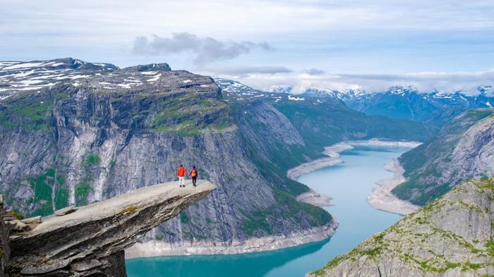 Due escursionisti si trovano sul bordo di Trolltunga, in Norvegia, una scogliera massiccia che si affaccia su un fiordo mozzafiato in Norvegia.