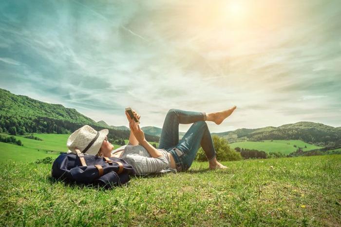 woman-holding-a-phone-lounging-on-sunny-grassy-hill-next-to-a-backpack-m.jpg