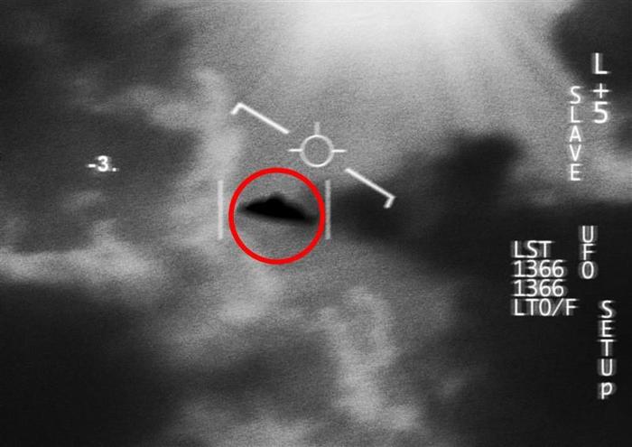 Una foto sfocata in bianco e nero che sembra essere stata scattata da una telecamera militare che segue un UFO nel cielo. L'oggetto a forma di disco è al centro dell'immagine circondato dalle nuvole. C'è un cerchio rosso intorno ad esso e dei segnalibri sul fotogramma per indicarne la posizione.