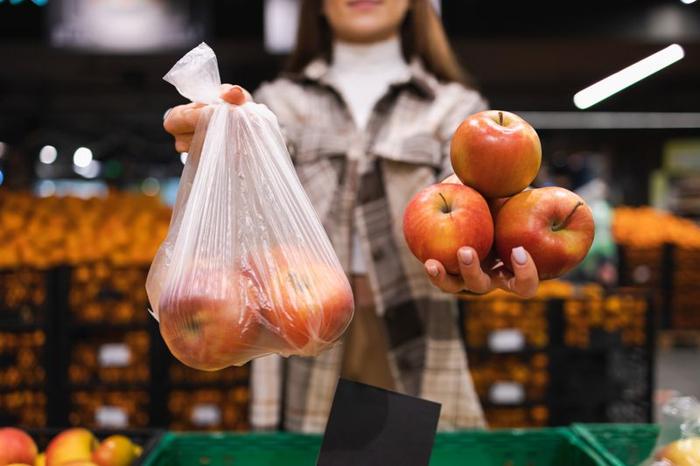 La donna sta pensando se prendere le mele in un sacchetto di plastica o farne a meno. La ragazza compra la frutta in un supermercato. Concetto di un mondo senza plastica