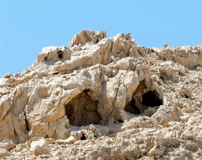 Una foto di una serie di grotte in una parete rocciosa di una scogliera. L'immagine mostra due delle grotte circondate da rocce pallide e frastagliate. La scena è completamente priva di qualsiasi vegetazione.