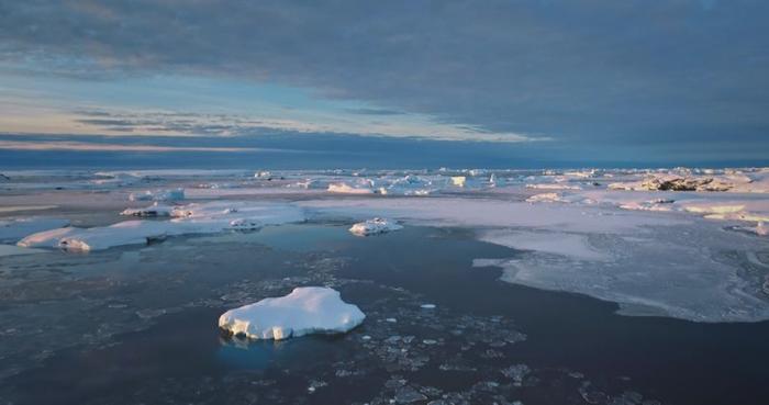 Costa antartica aerea al tramonto con banchi di ghiaccio, oceano e iceberg coperti di neve.