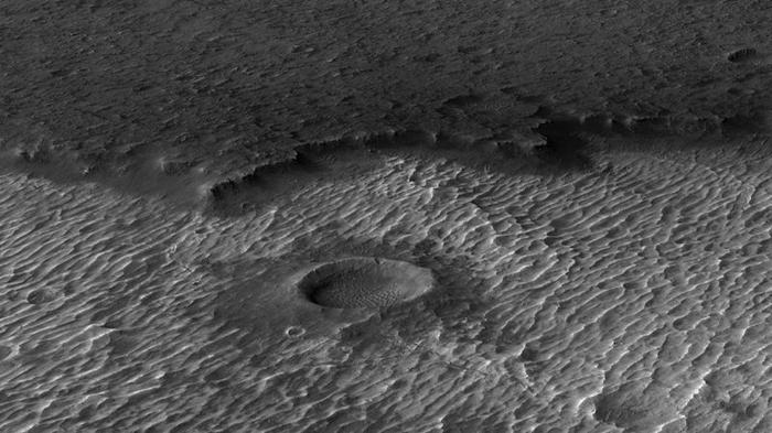 Una foto in bianco e nero mostra creste rocciose parallele, un grande cratere è visibile al centro