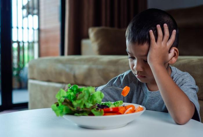 ragazzo giovane seduto al tavolo guardando triste mentre mangia un'insalata