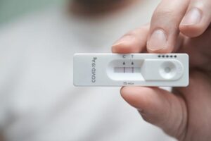 close up of hand holding rectangular white lateral flow kit with two lines, indicating a positive test for COVID-19