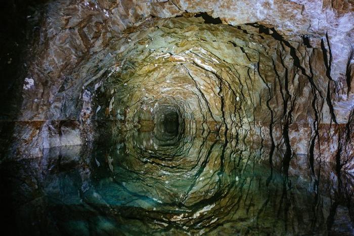 Galleria mineraria abbandonata buia allagata con riflessi d'acqua.