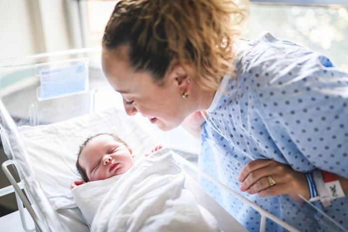 newborn baby sleeping in a hospital cot, mother looking over