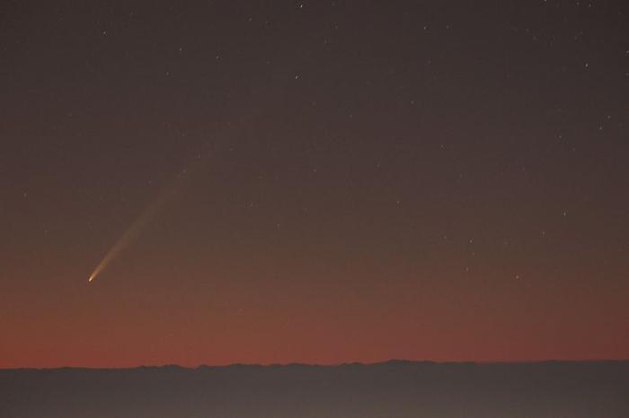 Il cielo è arancione come appena prima dell'alba. non troppo alto sull'orizzonte, la cometa e la sua coda sono chiaramente visibili. La coda è molto lunga e sottile