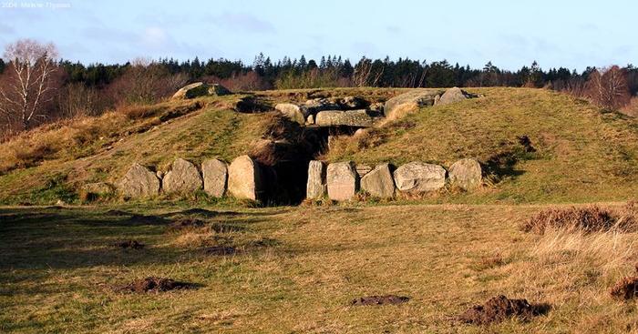 Una foto scattata presto la mattina di un dolmen della cultura del bicchiere a imbuto che mostra un tumulo terrestre con un ingresso che conduce al suo interno. L'ingresso ha quattro grandi pietre allineate sul lato destro e cinque pietre sul lato sinistro.