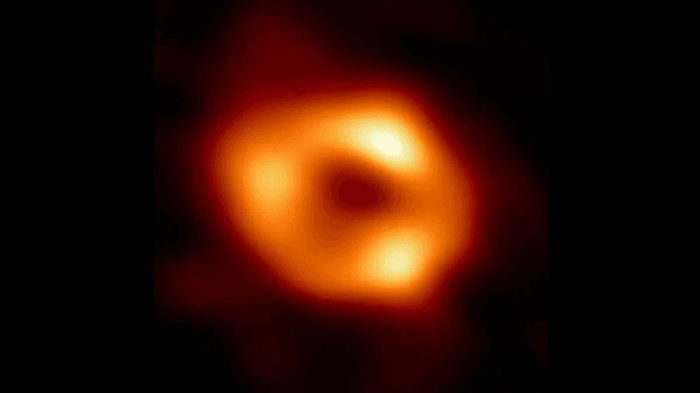 L'immagine del telescopio dell'orizzonte degli eventi del buco nero supermassiccio della nostra galassia, Sagittarius A*. Si vede un donut arancione con alcuni punti più luminosi intorno a un centro scuro dove si trova il buco nero