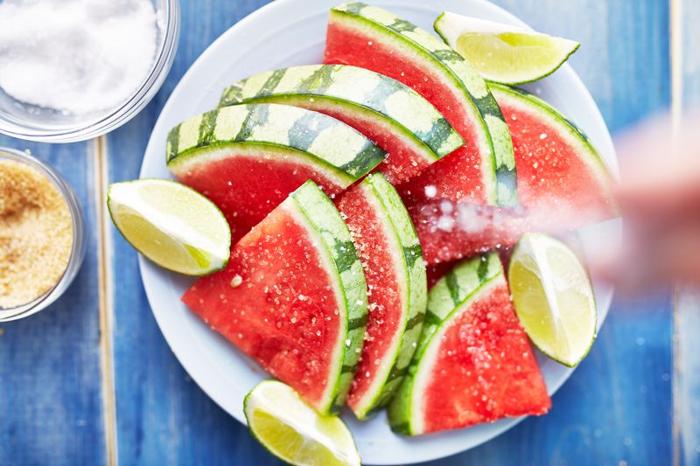 hand sprinkling salt on pile of watermelon slices