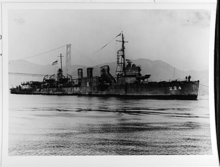 Una foto in bianco e nero che mostra l'USS Stewart in acqua con il Golden Gate Bridge sullo sfondo. L'acqua è calma e la nave aveva due membri dell'equipaggio in piedi sulla prua.