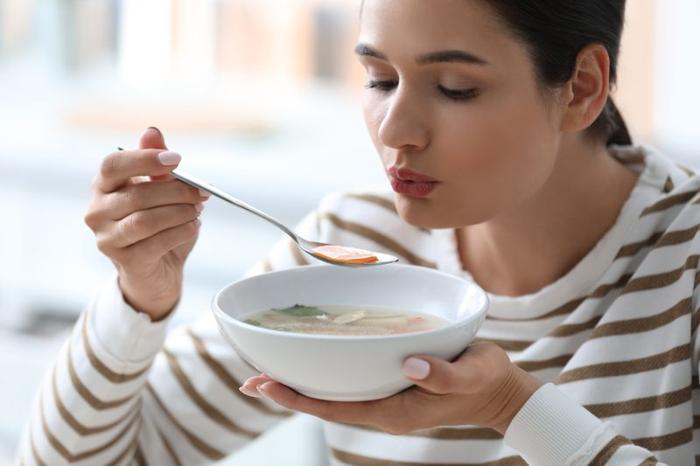 Donna che soffia su un cucchiaio di zuppa di verdure