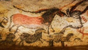 Una foto che mostra l'arte rupestre nella Grotta di Lascaux in Francia. L'immagine mostra un cavallo dipinto in rosso medio che viene sovrapposto al contorno nero di un grande animale simile a un toro. Sotto di esso ci sono rappresentazioni nere più piccole di altri animali simili a cavalli.