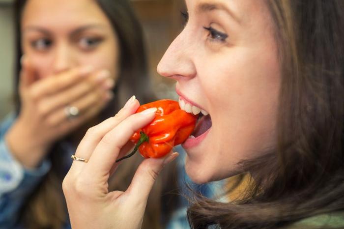 Una donna mangia un peperoncino rosso, mentre un amico scioccato guarda