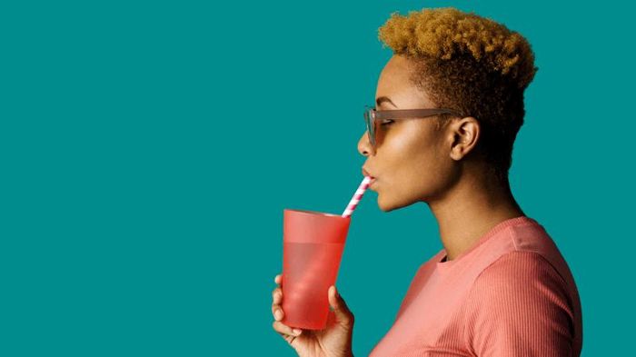 una donna che beve acqua da una tazza rossa attraverso una cannuccia