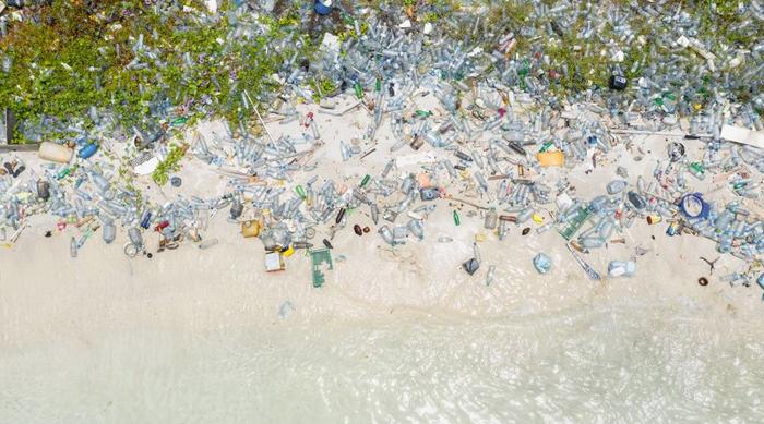 Una foto aerea che mostra masse di bottiglie di plastica spiaggiate. Il fondo dell'immagine mostra il bordo dell'acqua e la sabbia bianca, ma sopra questa linea ci sono migliaia di bottiglie e altre forme di plastica.