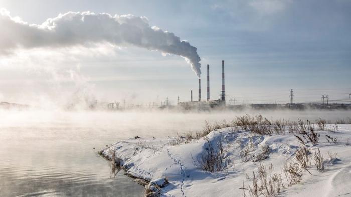 Vista della centrale termoelettrica di Zainskaya con cimini fumanti e un bacino senza ghiaccio con vapore che si alza dall'acqua in una giornata invernale e gelida di sole