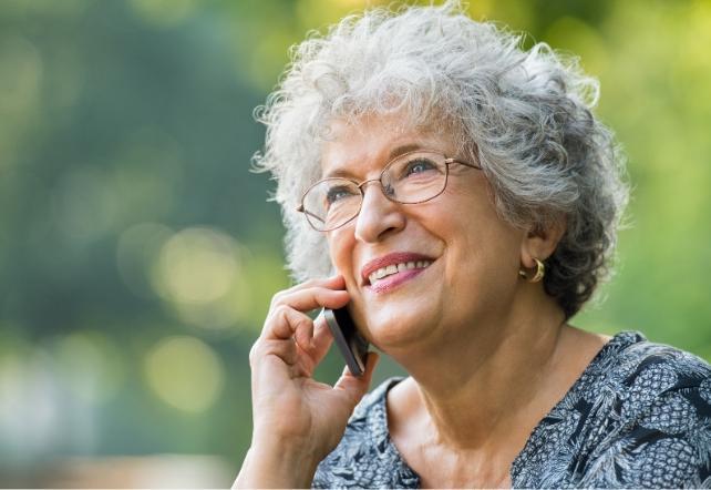 Una donna anziana con capelli grigi e occhiali, che parla al telefono