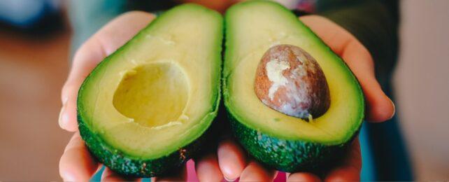 Mani che tengono un avocado tagliato a metà