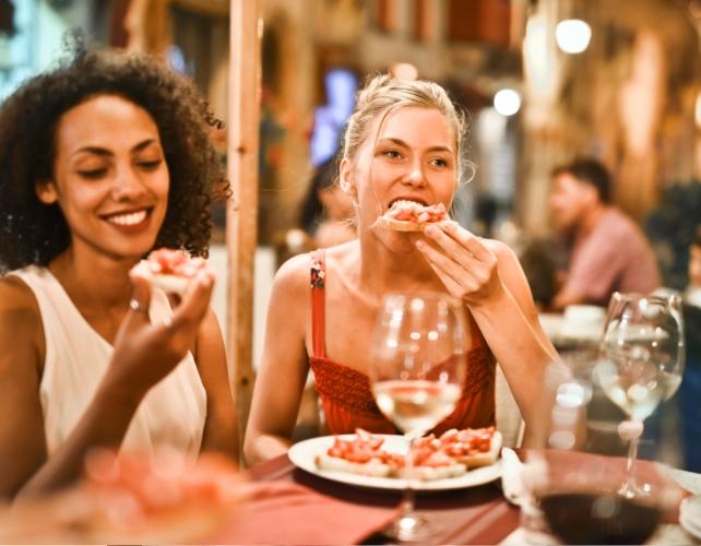 Due giovani donne mangiano pizza e bevono vino