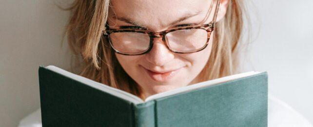 Persona con capelli biondi e occhiali che legge un libro