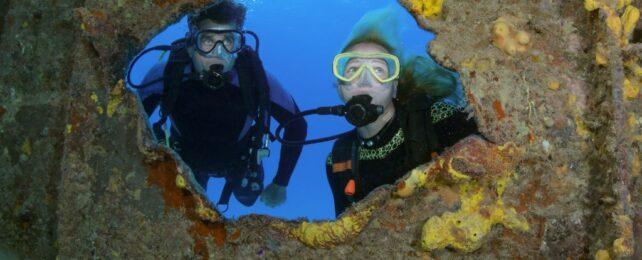 Due subacquei che guardano attraverso un buco nel relitto della nave