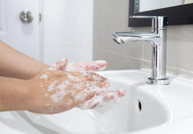 Mani saponose accanto a un rubinetto e un lavabo