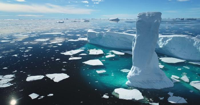 Enorme iceberg che si scioglie nell'oceano artico ghiacciato. Ghiacciaio coperto di neve alla deriva sotto un cielo blu e soleggiato. Puro ghiaccio galleggia in acqua turchese. Ecologia, scioglimento dei ghiacci, cambiamenti climatici e riscaldamento globale. Vista aerea