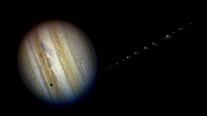 Giove è visto di lato con Io che proietta una piccola ombra su di esso. Sul lato si vedono piccoli frammenti sfocati che si trascinano, i frammenti della cometa che si avvicinano ai pianeti