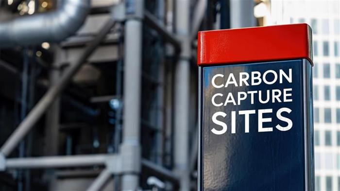 Un cartello che dice siti di cattura del carbonio, e dietro un sito industriale.