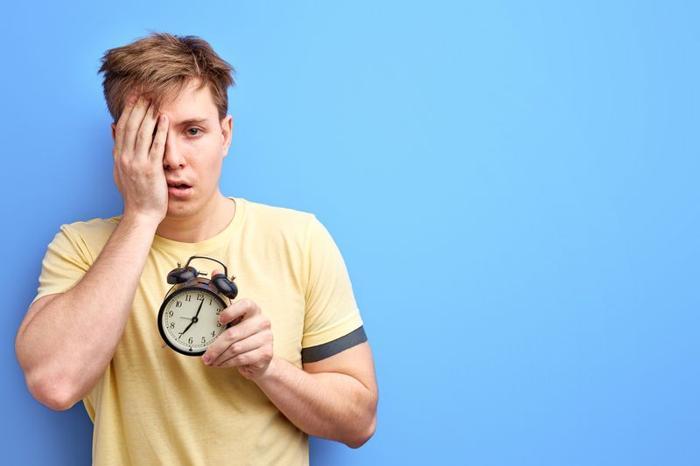 Uomo privo di sonno che tiene un orologio da sveglia