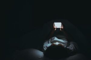 Donna con uno smartphone a letto al buio, lo schermo illumina il suo viso